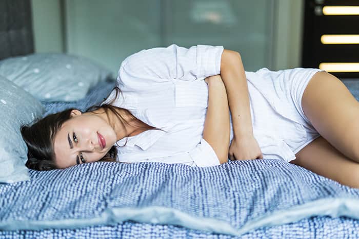 Impacto del estreñimiento crónico en la calidad de vida del paciente: young pretty woman in pain lying on bed min - HeelEspaña
